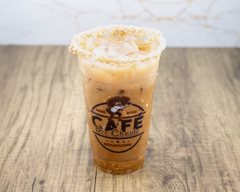 Iced horchata with a crushed cookie rim and Cafe Don Chente logo on a wooden table.