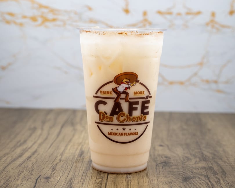 A Cafe Don Chente horchata drink with cinnamon on top, on a wooden table.